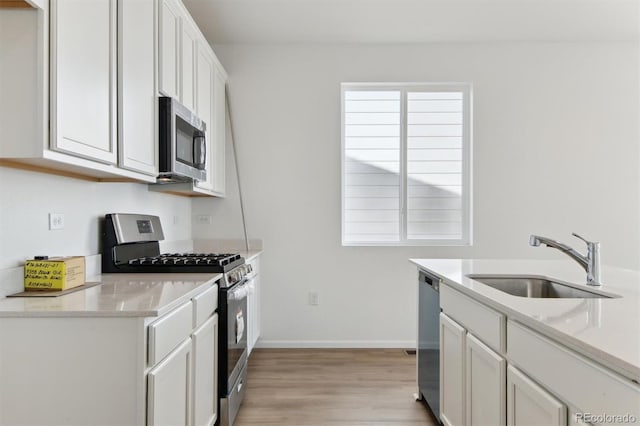 kitchen with white cabinets, sink, light hardwood / wood-style flooring, appliances with stainless steel finishes, and light stone counters