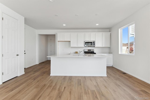 kitchen featuring sink, appliances with stainless steel finishes, a center island with sink, white cabinets, and light wood-type flooring