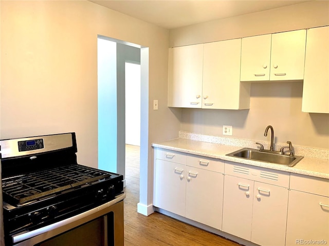 1143 Akron St, Aurora, CO 80010 - kitchen featuring gas stove, a sink, light countertops, light wood-type flooring, and white cabinetry