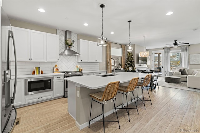 kitchen with light wood-type flooring, wall chimney range hood, sink, and appliances with stainless steel finishes