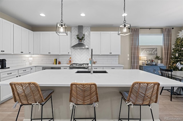 kitchen with white cabinets, light wood-type flooring, a kitchen island with sink, and wall chimney range hood