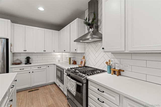 kitchen featuring white cabinetry, wall chimney exhaust hood, stainless steel appliances, and light hardwood / wood-style floors