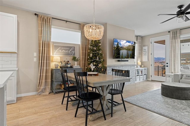 dining room featuring ceiling fan with notable chandelier, a fireplace, and light hardwood / wood-style flooring