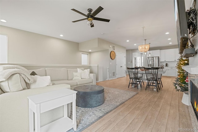 living room featuring ceiling fan with notable chandelier and light hardwood / wood-style floors