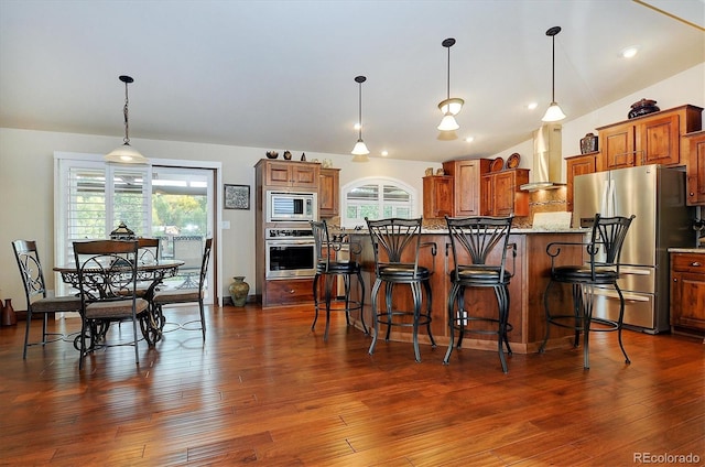 kitchen with a kitchen island, appliances with stainless steel finishes, wall chimney exhaust hood, and hanging light fixtures