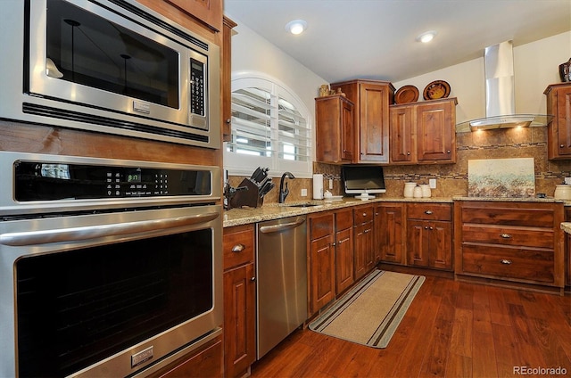 kitchen featuring light stone counters, dark wood-type flooring, wall chimney exhaust hood, stainless steel appliances, and tasteful backsplash