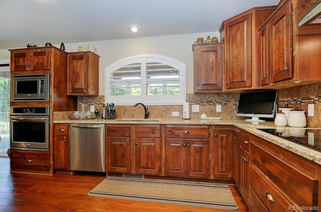 kitchen with stainless steel appliances, sink, light stone countertops, backsplash, and dark hardwood / wood-style floors