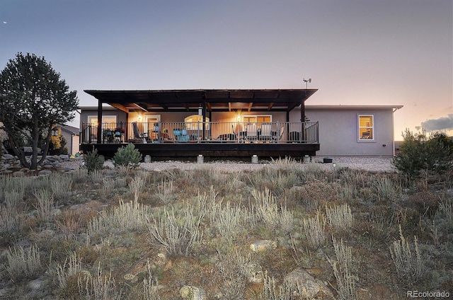 back house at dusk featuring a pergola and a deck