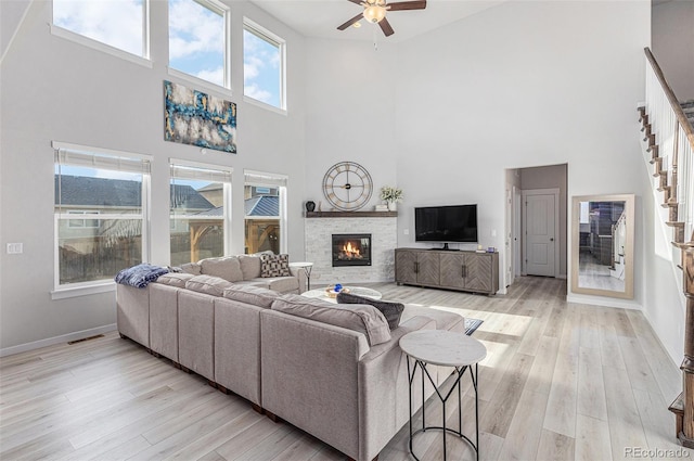 living area with light wood-style flooring, a fireplace, a ceiling fan, baseboards, and stairway