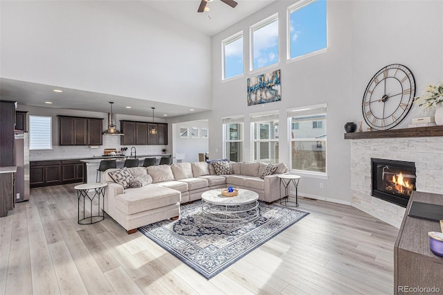 living area with ceiling fan, a stone fireplace, light wood finished floors, and baseboards