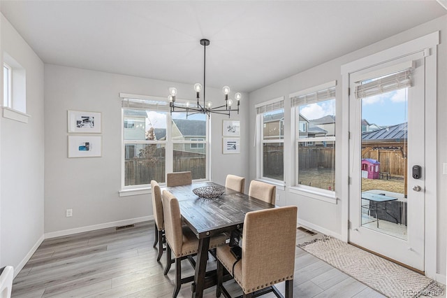 dining area with baseboards, light wood finished floors, a healthy amount of sunlight, and an inviting chandelier