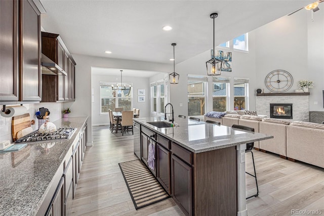 kitchen with dark brown cabinetry, stainless steel appliances, light wood-type flooring, a kitchen bar, and a sink