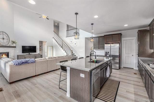 kitchen featuring a fireplace, stainless steel refrigerator with ice dispenser, a breakfast bar area, a sink, and dark brown cabinets