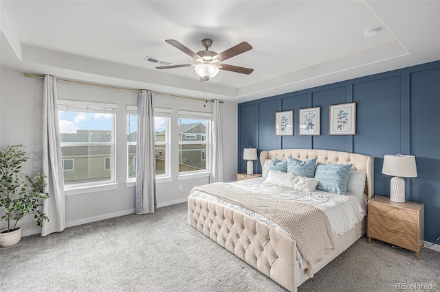 carpeted bedroom featuring a tray ceiling, visible vents, and baseboards