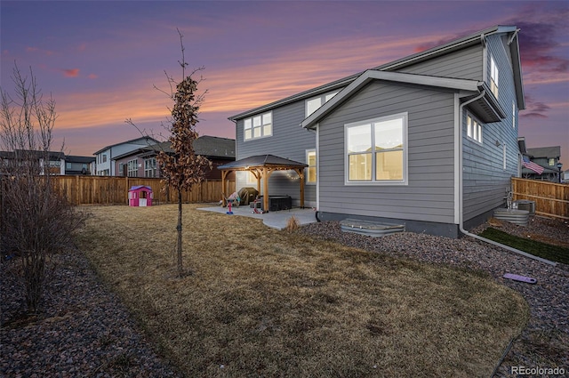 back of house at dusk featuring a gazebo, a lawn, a patio area, and a fenced backyard