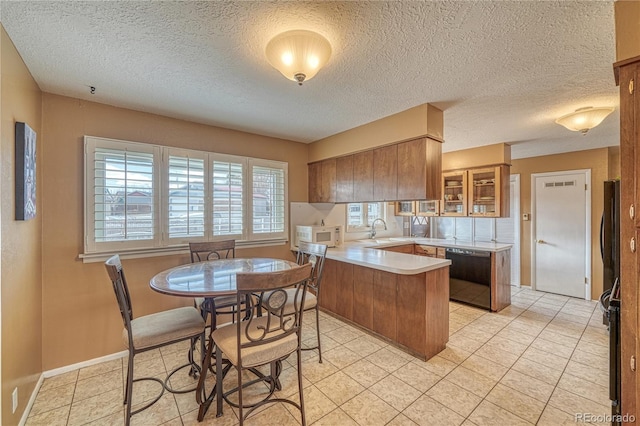 kitchen with brown cabinets, a sink, black dishwasher, a peninsula, and light countertops