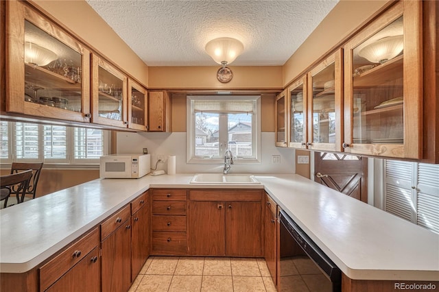 kitchen featuring a healthy amount of sunlight, white microwave, a peninsula, a sink, and light countertops