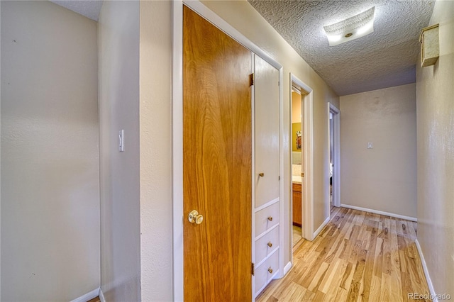 hallway featuring baseboards, a textured ceiling, and light wood finished floors