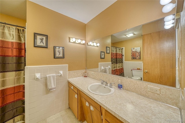 bathroom featuring curtained shower, toilet, vanity, wainscoting, and tile walls