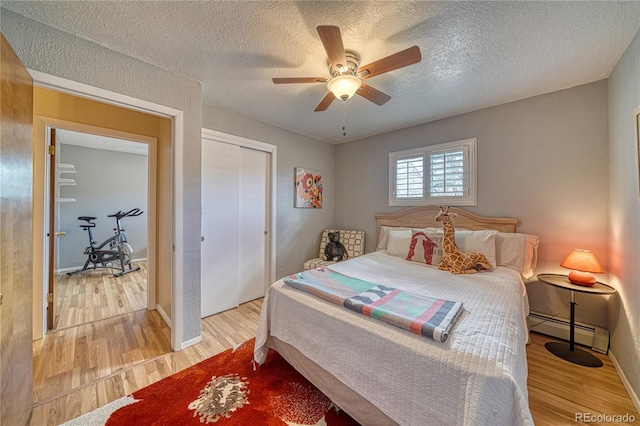 bedroom with a baseboard radiator, a closet, wood finished floors, and a ceiling fan