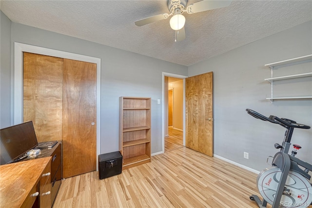 workout area featuring ceiling fan, light wood-style flooring, baseboards, and a textured ceiling