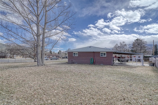 exterior space with brick siding, an attached carport, fence, a lawn, and metal roof