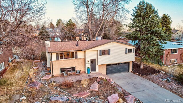 raised ranch with brick siding, driveway, a chimney, and an attached garage