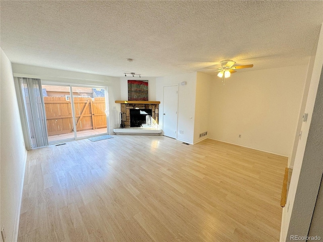 unfurnished living room with ceiling fan, a fireplace, light hardwood / wood-style floors, and a textured ceiling