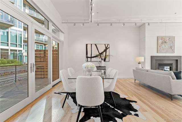 dining space with a glass covered fireplace, rail lighting, and light wood-type flooring