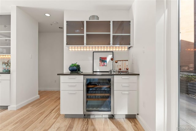 bar featuring wine cooler, light wood-style flooring, a bar, and baseboards