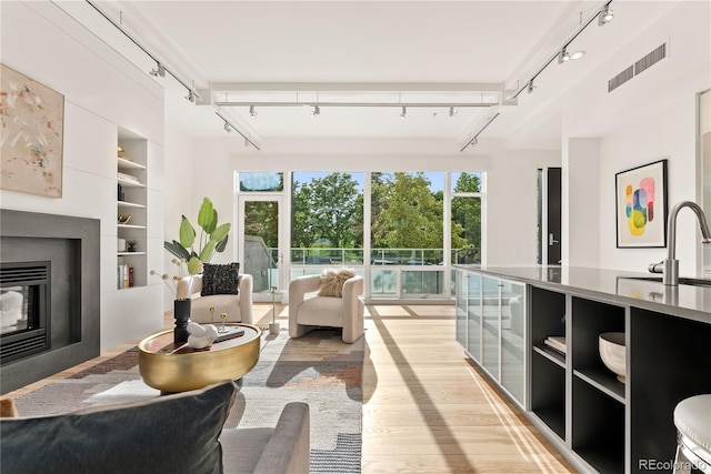 living room featuring built in shelves, visible vents, rail lighting, light wood-style floors, and a glass covered fireplace