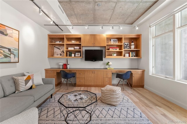 living area featuring track lighting, baseboards, built in desk, and light wood finished floors