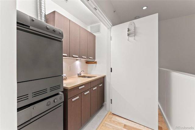 kitchen featuring visible vents, a sink, light countertops, stacked washer and clothes dryer, and wall oven