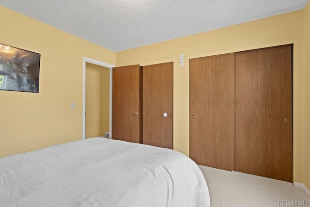 carpeted bedroom with two closets and a textured ceiling