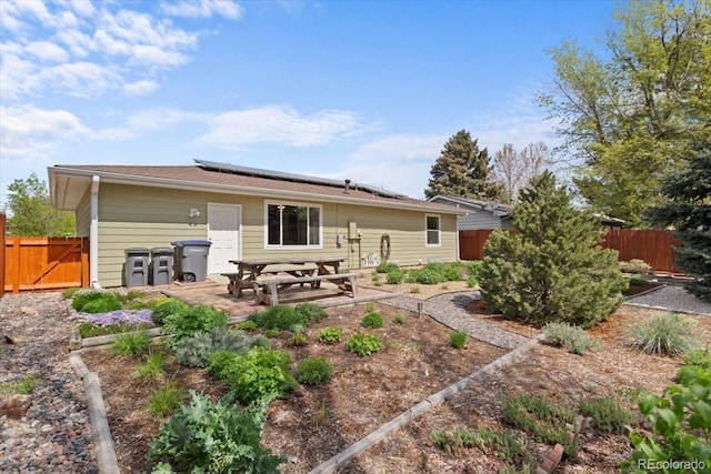 rear view of house featuring a fenced backyard, solar panels, and a patio area