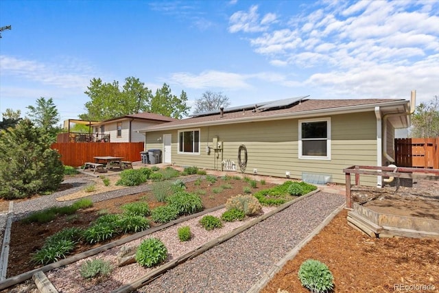 back of property featuring solar panels, a patio, fence, and a vegetable garden