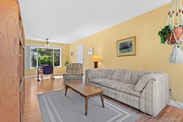 living room featuring baseboards, light wood-style flooring, and ceiling fan