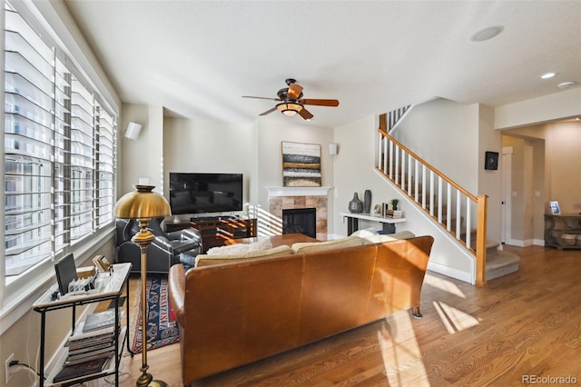 living room with a tiled fireplace, wood-type flooring, and ceiling fan