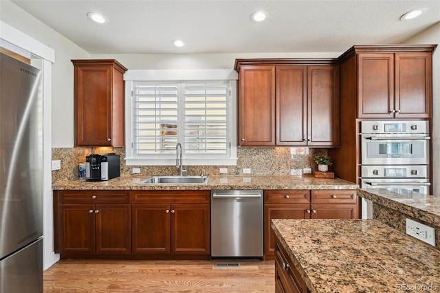 kitchen featuring appliances with stainless steel finishes, sink, decorative backsplash, and light wood-type flooring