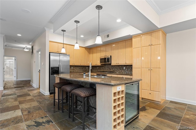 kitchen with light brown cabinets, a kitchen island with sink, dark stone counters, beverage cooler, and appliances with stainless steel finishes