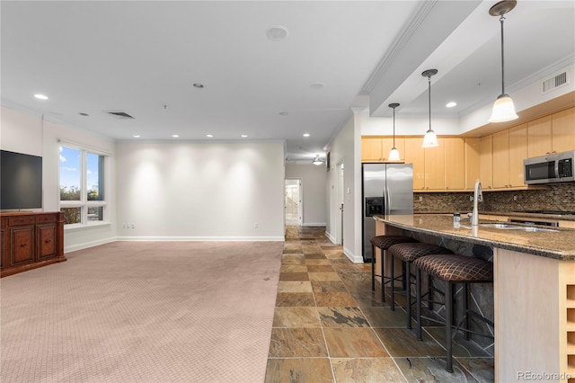 kitchen featuring light brown cabinets, dark colored carpet, hanging light fixtures, appliances with stainless steel finishes, and tasteful backsplash