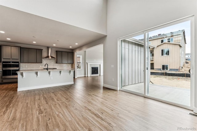 kitchen with wall chimney exhaust hood, tasteful backsplash, a breakfast bar area, and light hardwood / wood-style flooring