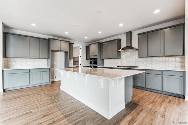 kitchen with a center island with sink, wall chimney exhaust hood, gray cabinetry, and light wood-type flooring