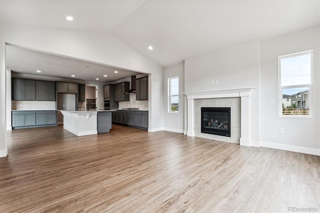 unfurnished living room with sink, light wood-type flooring, high vaulted ceiling, and a tiled fireplace