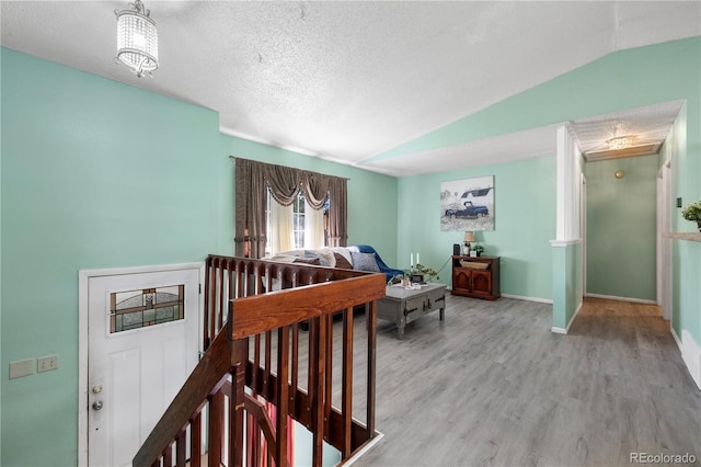 interior space featuring a textured ceiling, wood finished floors, an upstairs landing, baseboards, and vaulted ceiling