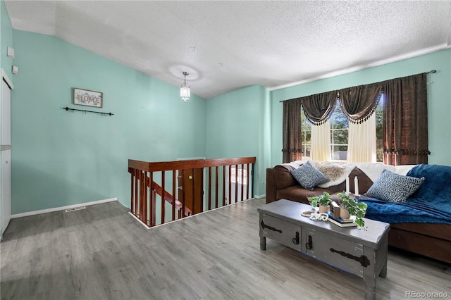 sitting room with baseboards, wood finished floors, vaulted ceiling, a textured ceiling, and an upstairs landing