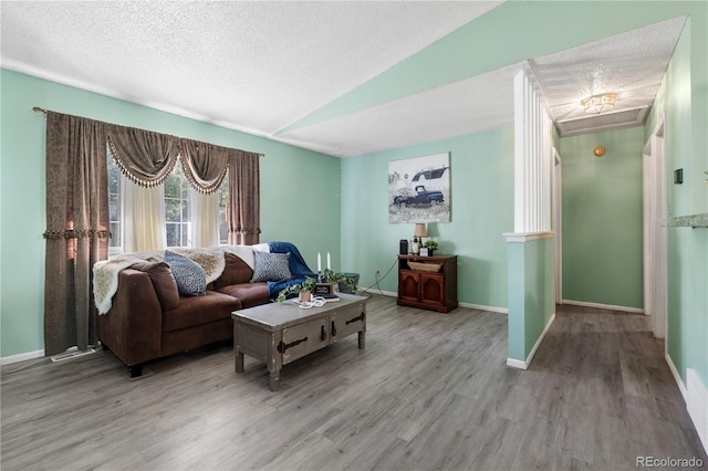 living room featuring lofted ceiling, a textured ceiling, baseboards, and wood finished floors