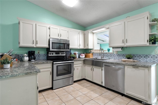 kitchen featuring lofted ceiling, stainless steel appliances, a sink, and white cabinetry