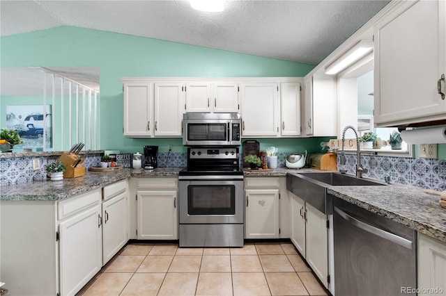 kitchen featuring light tile patterned floors, appliances with stainless steel finishes, vaulted ceiling, white cabinetry, and a sink