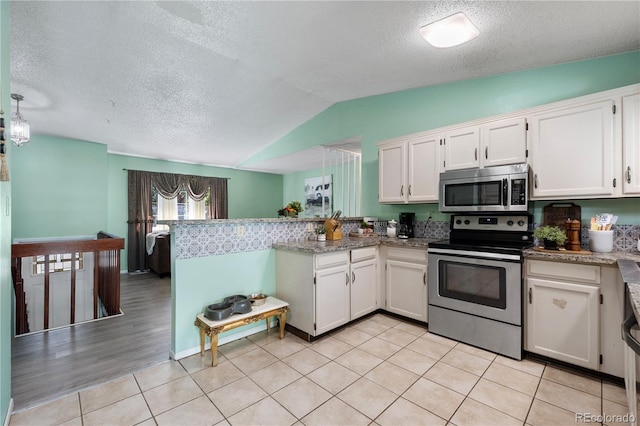 kitchen with light tile patterned floors, stainless steel appliances, lofted ceiling, white cabinets, and a peninsula